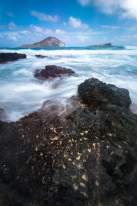 Scenic view of waves splashing on rocks against sky