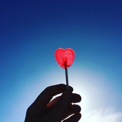 Cropped image of hand holding lollipop against clear blue sky