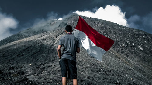 Rear view of man standing on mountain against sky