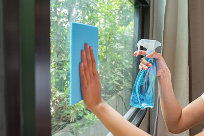 Midsection of woman photographing through smart phone on window