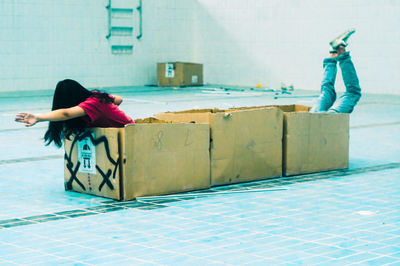 Playful friends playing with cardboard boxes on tiled floor