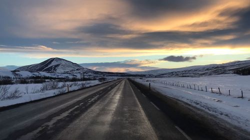 Empty road by snowcapped mountains against sky during sunset