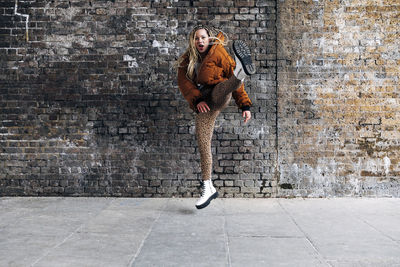 Full length of woman jumping against brick wall