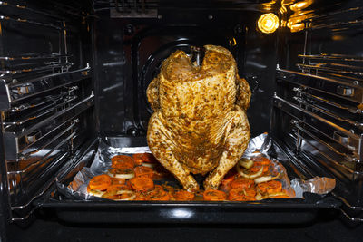 Raw chicken stuffed on an open beer bottle, lying on a baking tray with carrots and onions  oven.