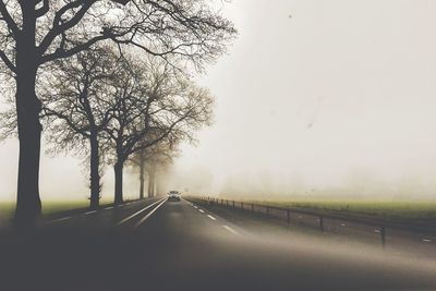 Road amidst trees against sky during foggy weather