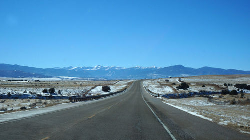 Country road leading towards mountains against blue sky