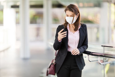 Full length of woman holding mobile phone standing outdoors