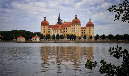 View of buildings by river against cloudy sky