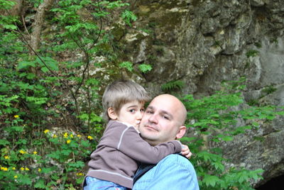 Portrait of son kissing father on cheek against plants