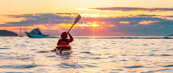 Rear view of woman in sea against sky during sunset