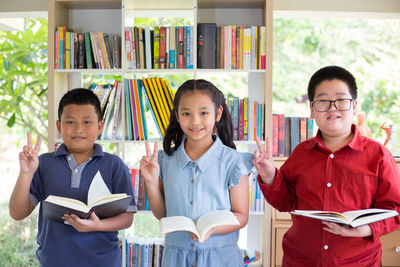 Portrait of smiling students with books showing peace sign in library