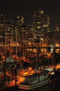 Illuminated sailing boat moored at harbor against buildings in city at night