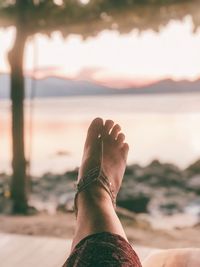 Low section of woman wearing jewelry at beach during sunset