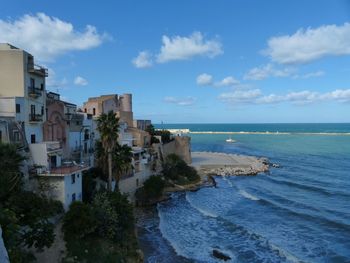 Buildings by sea against blue sky