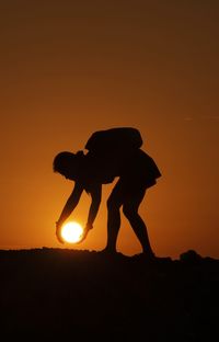 Silhouette man standing on field against orange sky