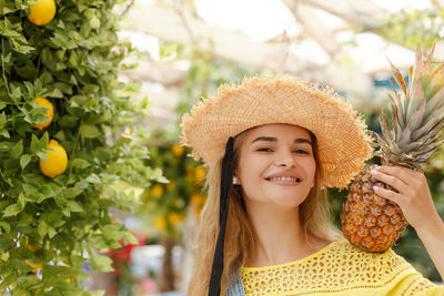 Cheerful beautiful girl in a straw hat holds a pineapple. yellow lemons on the background. summer
