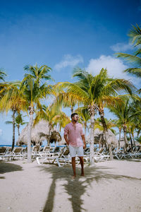 Man standing by palm tree on beach against sky