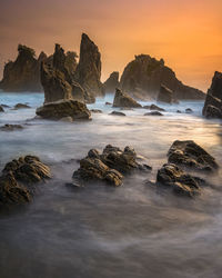 Rocks in sea against sky during sunset