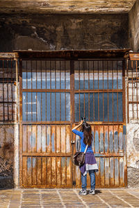 Rear view of woman photographing old metallic gate