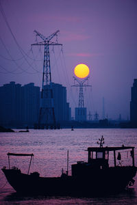 Silhouette buildings by sea against sky during sunset