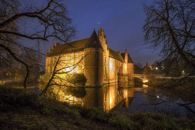 Bare trees by historic building against sky at night