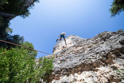 Low angle view of male friends climbing on mountain against clear blue sky