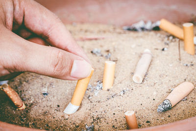 Close-up of hand holding cigarette butt in sand