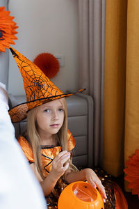 Portrait of cute girl wearing witch hat siting at home