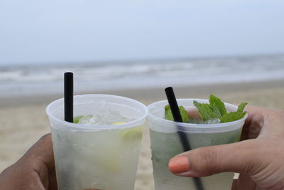 Close-up of hand holding drink against sea