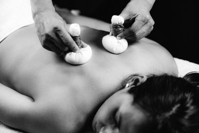 Hands of an ayurveda massage therapist pressing herbal bolus bags onto clients skin