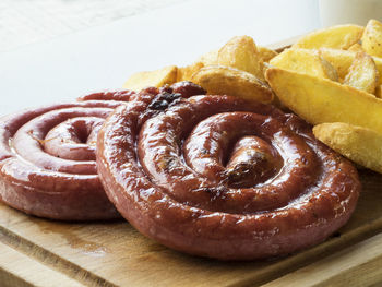 High angle view of fresh curled sausages with potato wedges on serving board