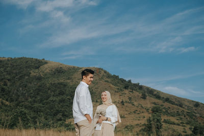 Couple standing on landscape against sky