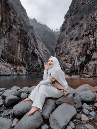 Rear view of woman sitting on rock by lake