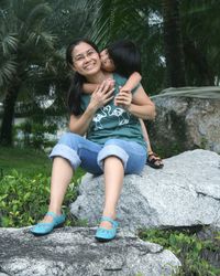 Portrait of happy mother and boy sitting on rock against trees