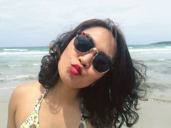 Close-up of young woman puckering at beach against sky