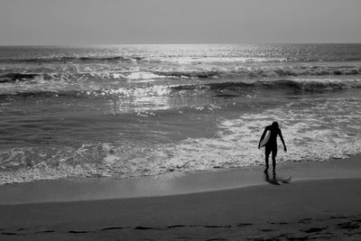 Rear view of silhouette man walking on beach against clear sky