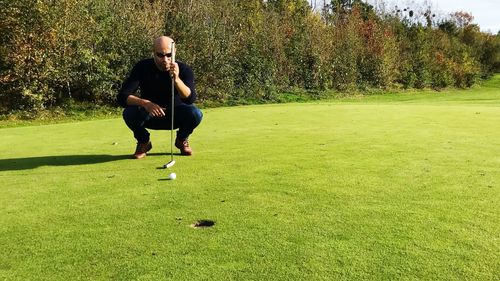 Full length of man holding club while crouching on golf course