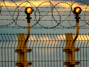 Low angle view of barbed wire against cloudy sky during sunset