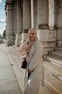 Portrait of young woman standing against building in city