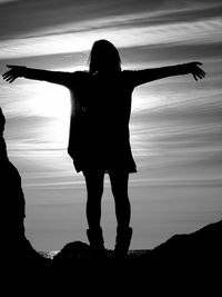 Silhouette of girl standing with arms outstretched against sun