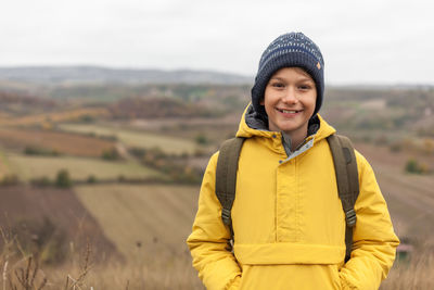 Happy elementary boy standing in nature during autumn day and looking at camera. copy space.