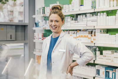 Happy pharmacist with hand on hip standing in chemist shop