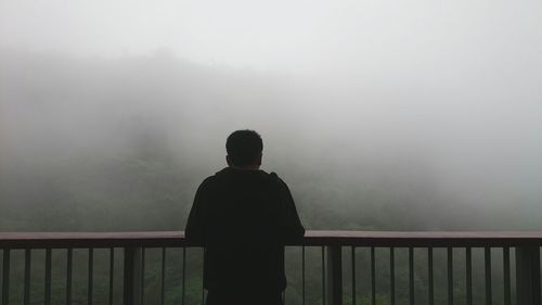 Rear view of man standing on observation point against foggy weather