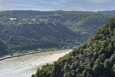 The river rhine in western germany flows between the hills covered with forest, buildings visible.