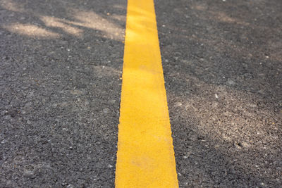 Yellow line on concrete road with rough surface under sunlight in the park shows concept of sign 