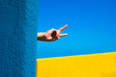 Person hand against yellow wall against clear blue sky