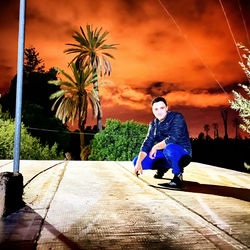 Man standing on footpath by palm trees against sky