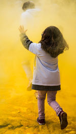 Rear view of girl enjoying with yellow powder paint