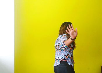 Woman showing stop gesture against yellow wall