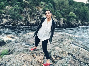 Portrait of smiling young woman standing on rock formation against river